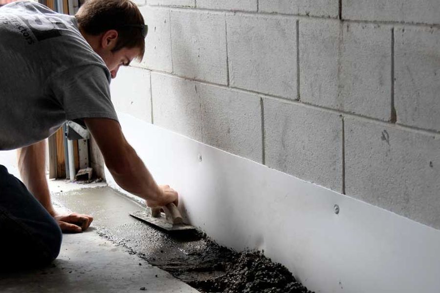 Worker applying waterproofing treatment along a foundation wall